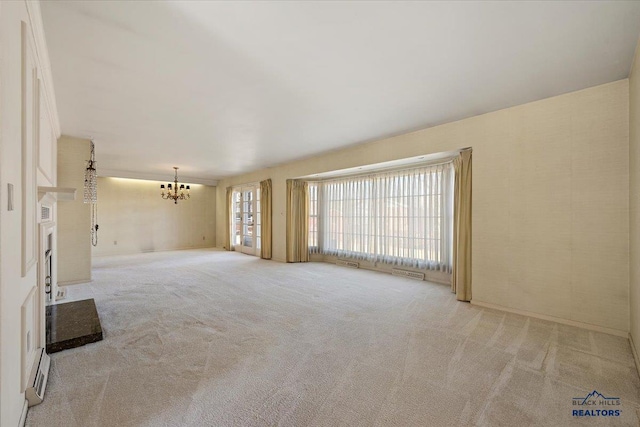 unfurnished living room with a fireplace with raised hearth, carpet floors, and an inviting chandelier