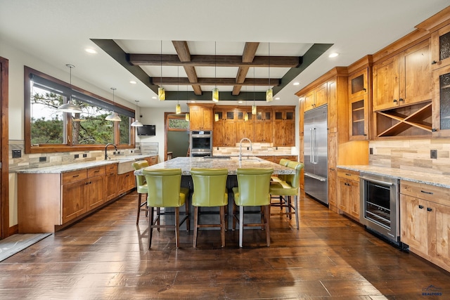 kitchen with a breakfast bar area, a kitchen island with sink, beverage cooler, coffered ceiling, and built in refrigerator