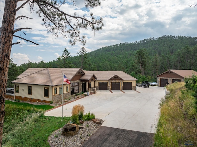 view of front of property featuring concrete driveway, stone siding, a wooded view, and a tile roof