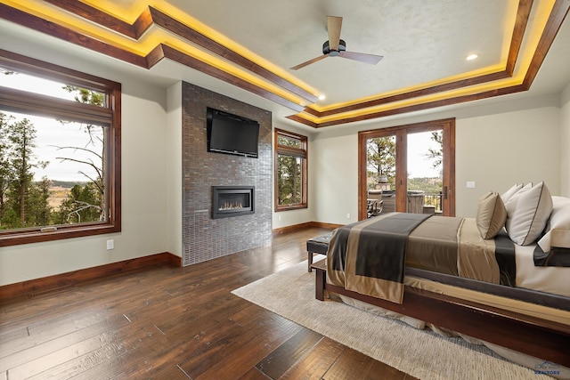 bedroom with a large fireplace, baseboards, a raised ceiling, dark wood finished floors, and access to exterior