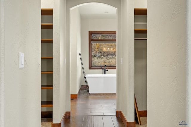 corridor featuring arched walkways, a textured wall, baseboards, and wood tiled floor