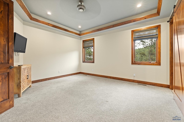 empty room featuring light carpet, a barn door, visible vents, and a tray ceiling