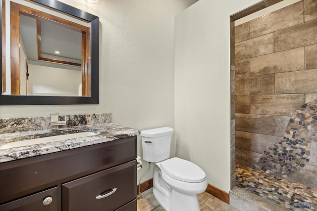 bathroom featuring toilet, baseboards, a tile shower, and vanity