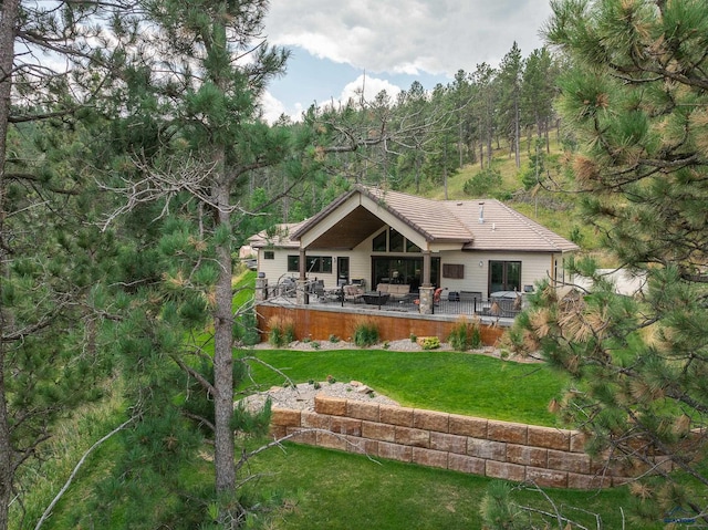 back of house featuring a tiled roof, a lawn, and a view of trees