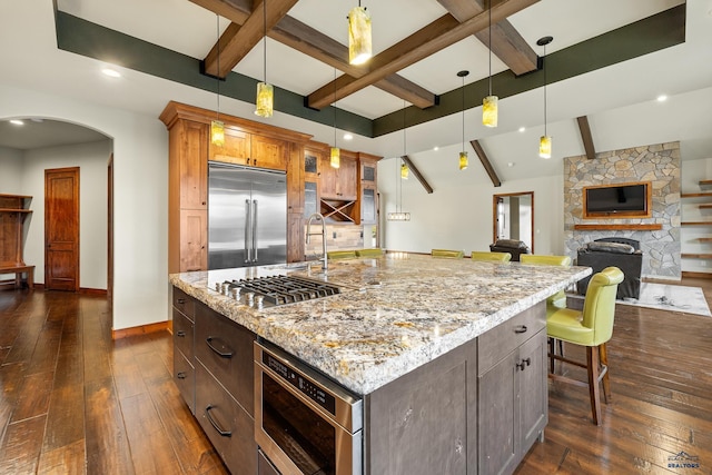 kitchen featuring arched walkways, light stone counters, baseboards, appliances with stainless steel finishes, and dark wood finished floors