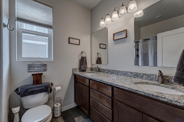 bathroom with double vanity, a sink, toilet, and wood finished floors