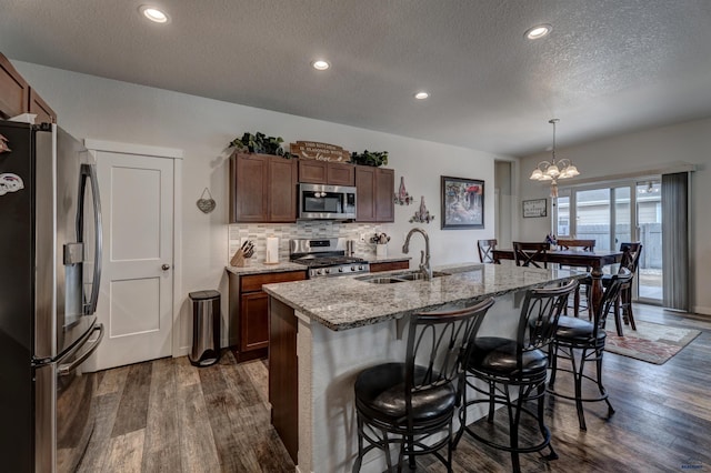 kitchen featuring a breakfast bar, a sink, appliances with stainless steel finishes, light stone countertops, and dark wood-style floors