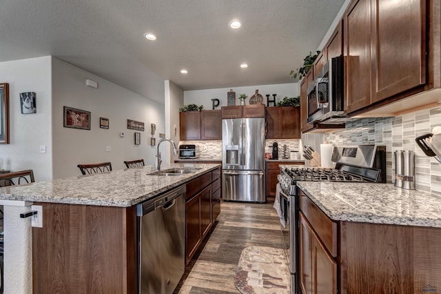 kitchen with a center island with sink, appliances with stainless steel finishes, a breakfast bar, dark wood-style flooring, and a sink