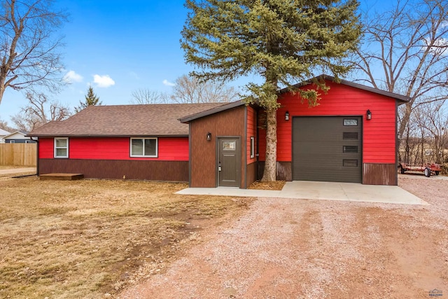 view of front of home with roof with shingles, dirt driveway, an attached garage, fence, and an outdoor structure