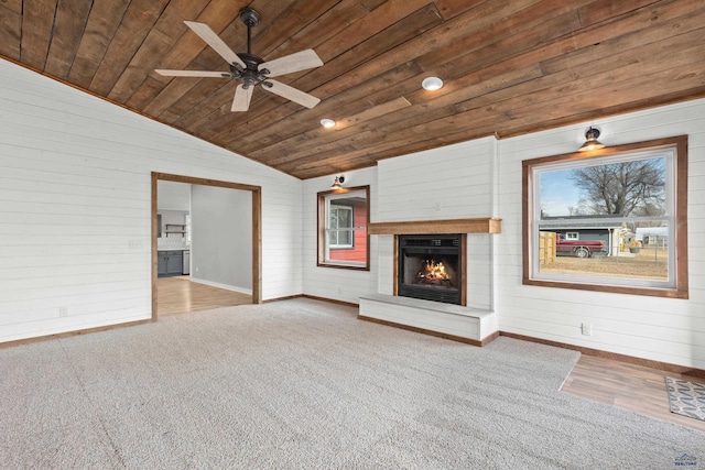 unfurnished living room featuring baseboards, a ceiling fan, wood ceiling, a lit fireplace, and vaulted ceiling