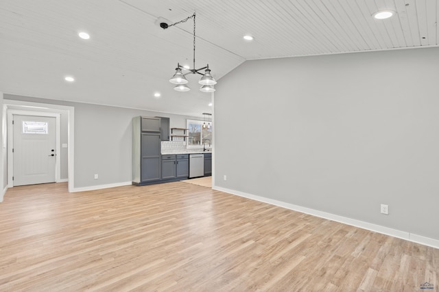 unfurnished living room with light wood-type flooring, a notable chandelier, lofted ceiling, and baseboards