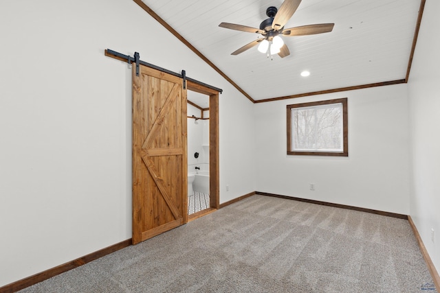 unfurnished bedroom featuring carpet floors, lofted ceiling, a barn door, ornamental molding, and baseboards