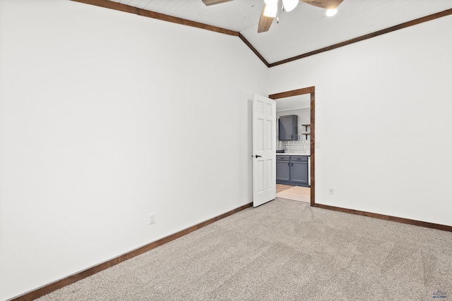 spare room with crown molding, lofted ceiling, light colored carpet, a ceiling fan, and baseboards