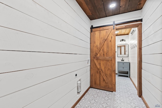 corridor featuring wooden ceiling, a barn door, and wooden walls