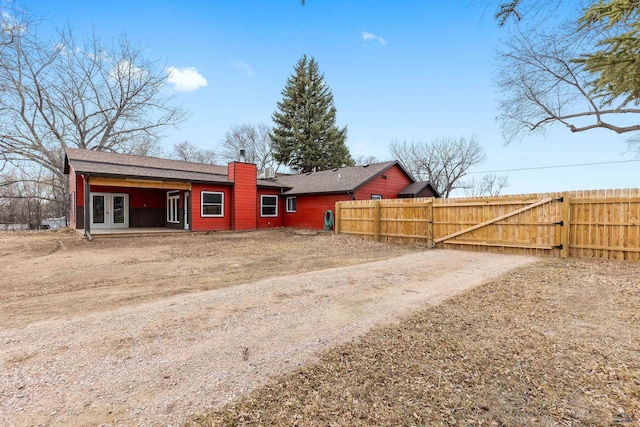 rear view of house with dirt driveway, a chimney, fence, and french doors