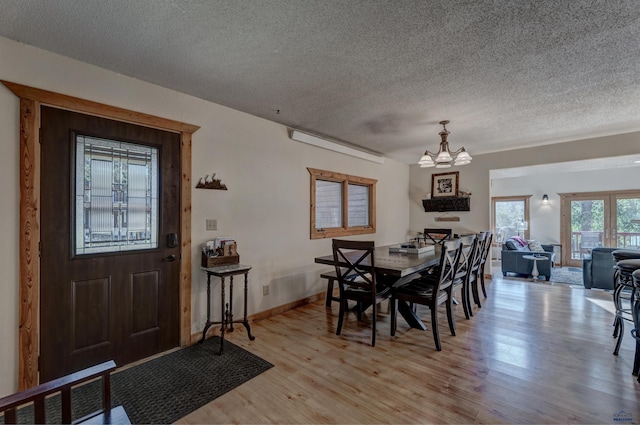 dining space with baseboards, light wood-style flooring, a chandelier, and a textured ceiling