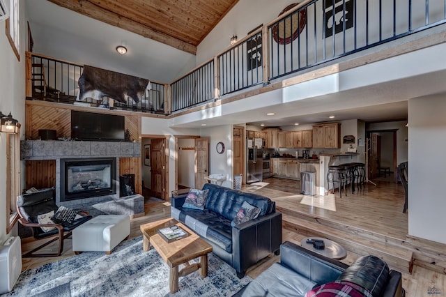 living room with high vaulted ceiling, light wood-type flooring, a tile fireplace, and wood ceiling