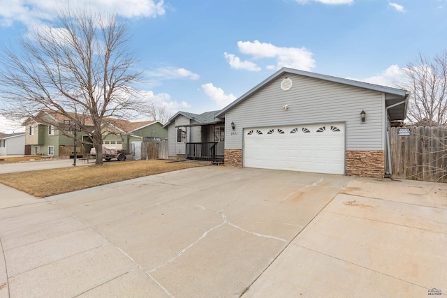 view of front of property with an attached garage, stone siding, concrete driveway, and fence