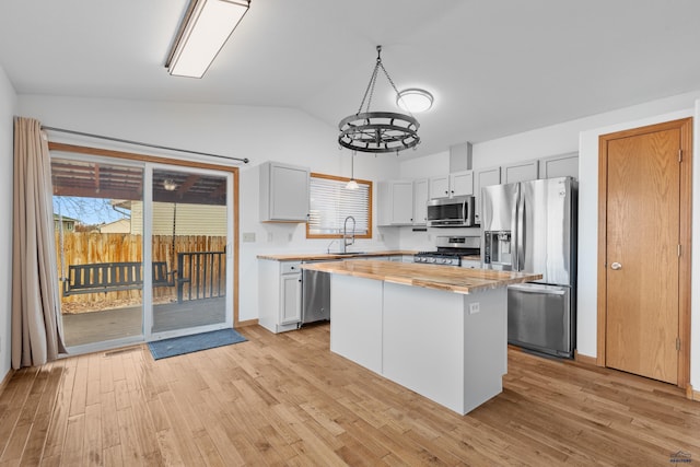 kitchen with lofted ceiling, a kitchen island, appliances with stainless steel finishes, light wood-type flooring, and a sink