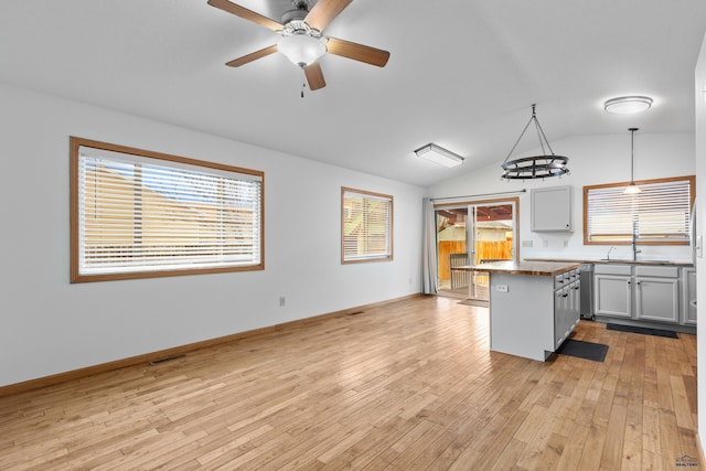 kitchen featuring decorative light fixtures, lofted ceiling, stainless steel dishwasher, open floor plan, and light wood-type flooring