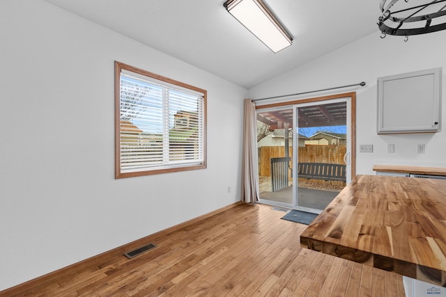 unfurnished dining area featuring visible vents, vaulted ceiling, light wood-style flooring, and baseboards