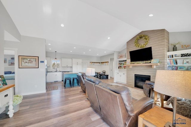 living room with a large fireplace, light wood-style flooring, vaulted ceiling, and recessed lighting