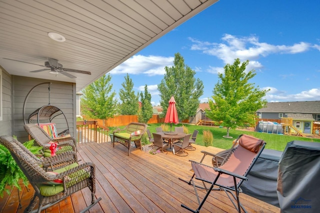 wooden terrace featuring a ceiling fan, outdoor dining space, a lawn, and fence