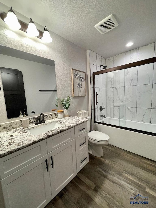 full bath featuring visible vents, toilet, enclosed tub / shower combo, a textured ceiling, and wood finished floors