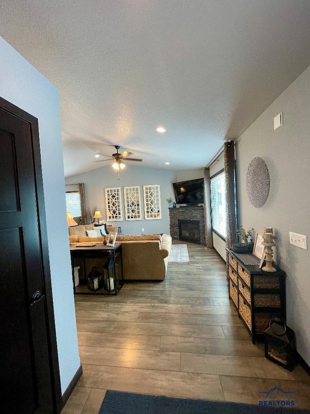 living room featuring lofted ceiling, a textured ceiling, a fireplace, wood finished floors, and a ceiling fan