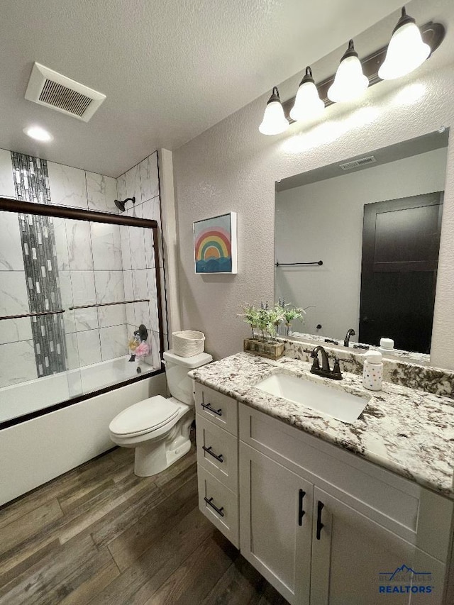 full bath featuring visible vents, toilet, shower / bath combination with glass door, wood finished floors, and a textured ceiling