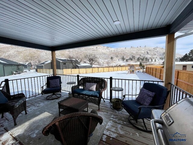 snow covered deck with a fenced backyard, a mountain view, and grilling area