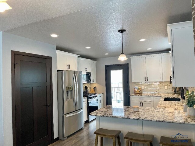 kitchen featuring stainless steel appliances, a peninsula, a sink, white cabinetry, and light stone countertops