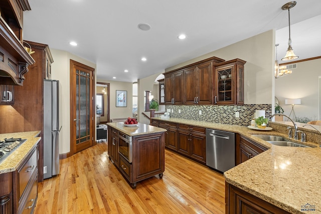 kitchen with decorative light fixtures, light wood finished floors, stainless steel appliances, visible vents, and a sink