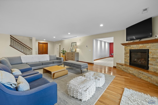 living room featuring a stone fireplace, recessed lighting, wood finished floors, visible vents, and baseboards