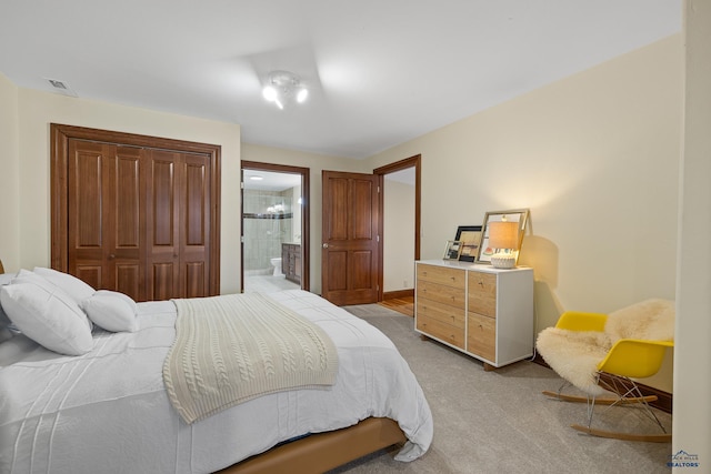 bedroom with a closet, light colored carpet, visible vents, ensuite bathroom, and baseboards