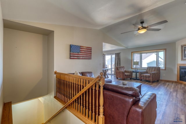 living room with lofted ceiling, ceiling fan, wood finished floors, baseboards, and a glass covered fireplace