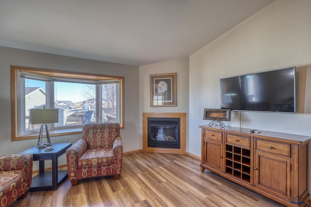living room featuring light wood-type flooring, a glass covered fireplace, and baseboards