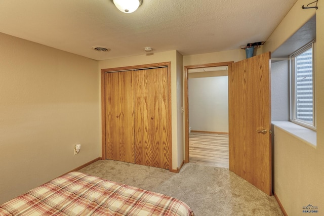 unfurnished bedroom featuring baseboards, visible vents, carpet, a textured ceiling, and a closet
