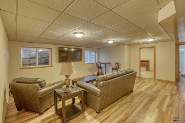 living room with a drop ceiling, light wood-style flooring, and baseboards