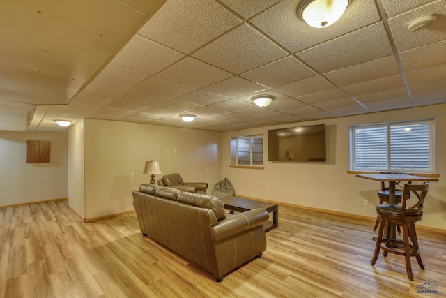 living area with a drop ceiling, light wood-type flooring, and baseboards