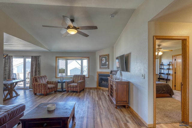living area with light wood-type flooring, ceiling fan, baseboards, and a glass covered fireplace