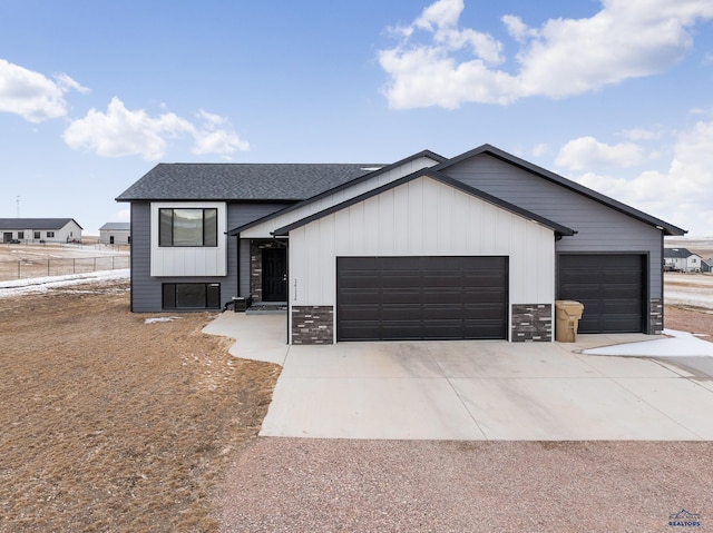 view of front facade featuring an attached garage, a shingled roof, fence, driveway, and stone siding