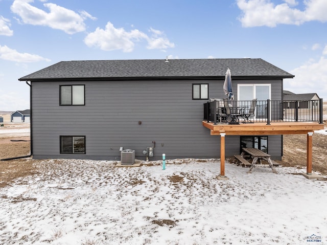 snow covered property featuring central air condition unit, a deck, and roof with shingles