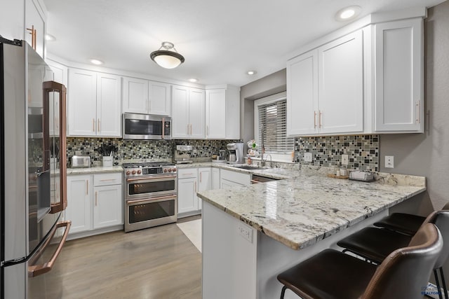 kitchen with a peninsula, a sink, white cabinetry, appliances with stainless steel finishes, and light wood finished floors