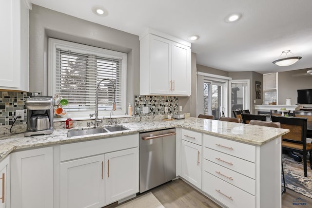 kitchen with a peninsula, a sink, white cabinetry, stainless steel dishwasher, and tasteful backsplash