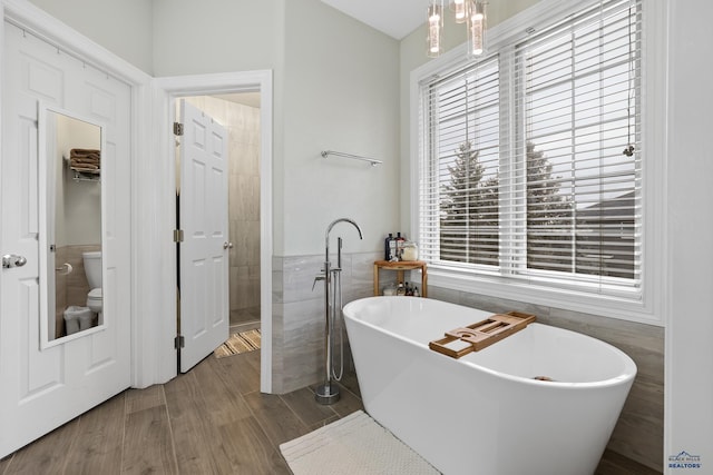 bathroom with tile walls, a freestanding bath, toilet, wainscoting, and wood finished floors