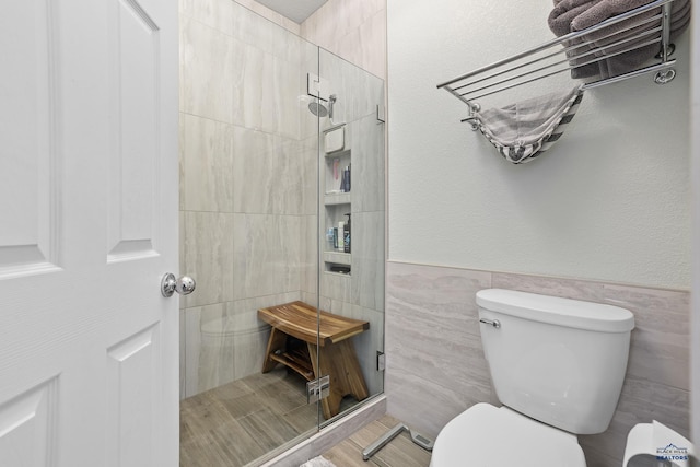 full bathroom with a wainscoted wall, a shower stall, toilet, and tile walls