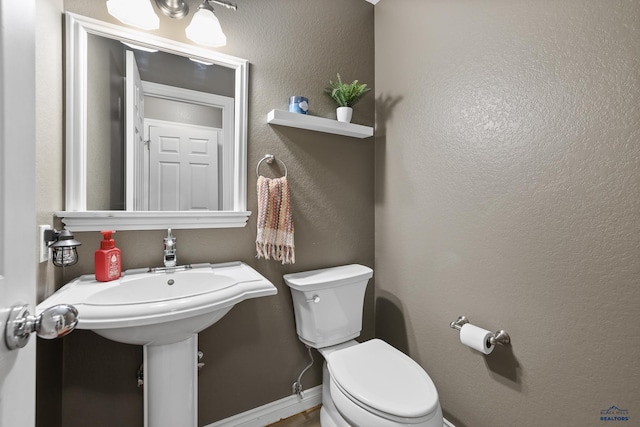 bathroom featuring toilet, baseboards, and a textured wall