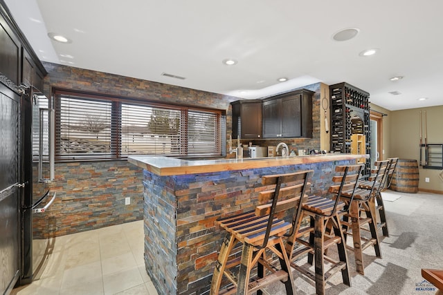 kitchen featuring dark brown cabinetry, visible vents, a breakfast bar area, a peninsula, and a sink