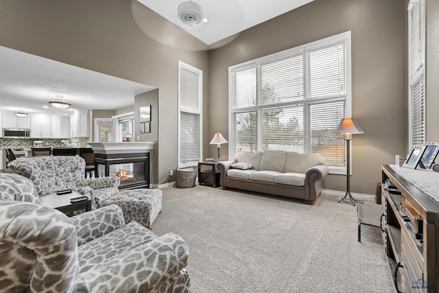 living area with baseboards, light carpet, ceiling fan, and a multi sided fireplace